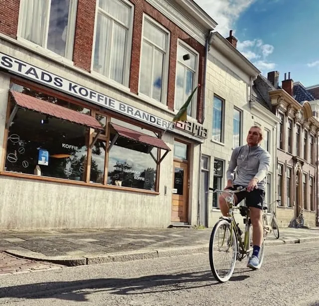 man on bike cycling in old European town next to coffee shop